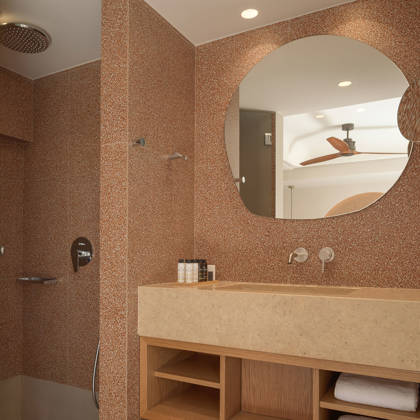 Salle de bain de chambre Deluxe avec vasque en pierre, miroir rond et douche à l'italienne