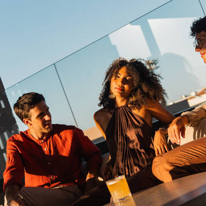 Trois clients discutent autour d'un verre au rooftop lounge dans la lumière dorée
