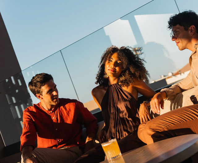 Three guests chatting over drinks at the rooftop lounge in the golden light