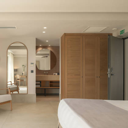 Suite Junior avec armoire en bois, vasque ouverte, fauteuil et grand miroir arqué