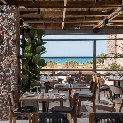 Salle de restaurant avec poutres en bois, colonne en pierre et tables dressées face à la mer 