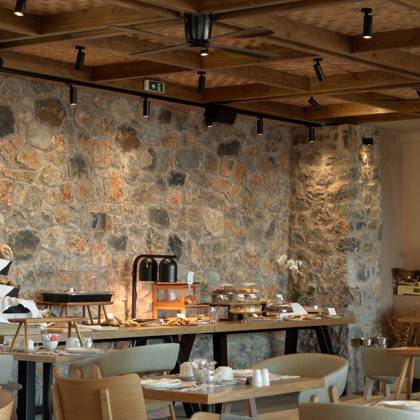 Buffet du petit-déjeuner le long d'un mur en pierre, tables dressées sous poutres en bois