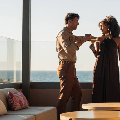 Un couple trinque avec des cocktails au rooftop lounge, la mer en arrière-plan