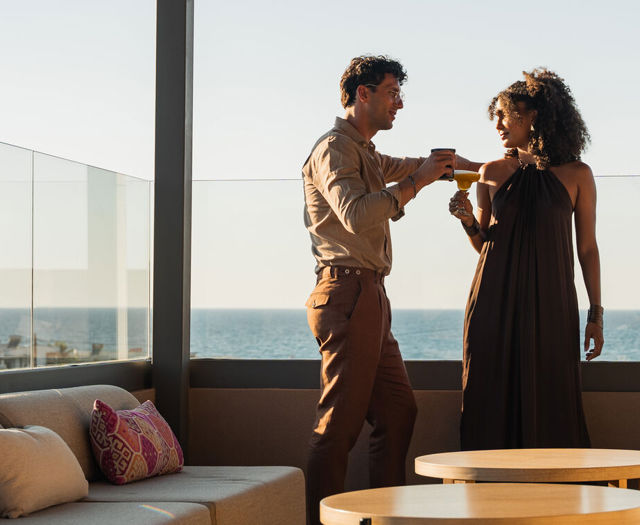 Couple toasting with cocktails at the rooftop lounge with the sea behind them