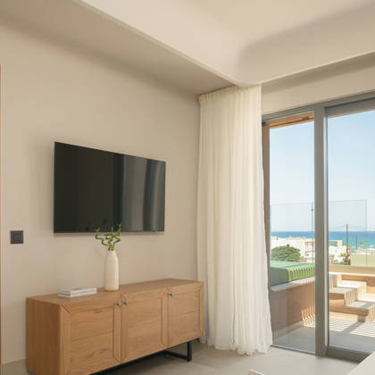 Salon de la suite avec télévision, buffet et porte de terrasse avec vue mer, chambre attenante