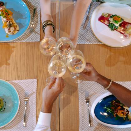 Convives trinquant au vin blanc au-dessus d'une table garnie de plats à la carte colorés