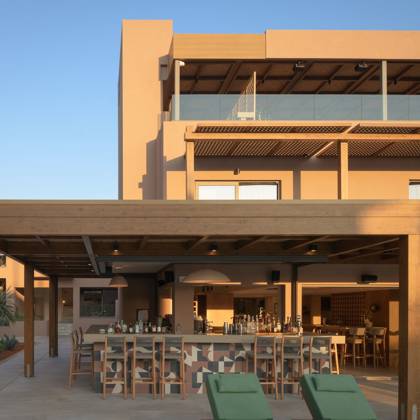 Bar en plein air sous une pergola en bois avec transats verts à la lumière du soir