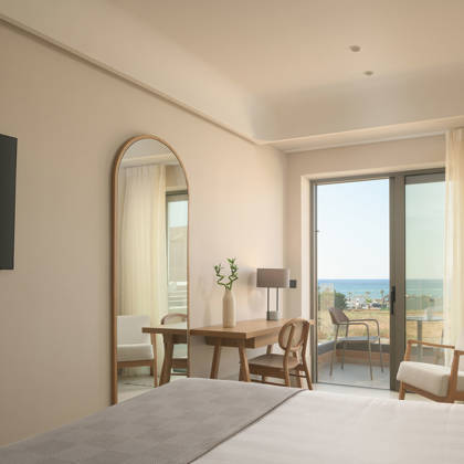 Suite Junior avec bureau en bois, miroir arqué et télévision, ouvrant sur un balcon avec vue mer