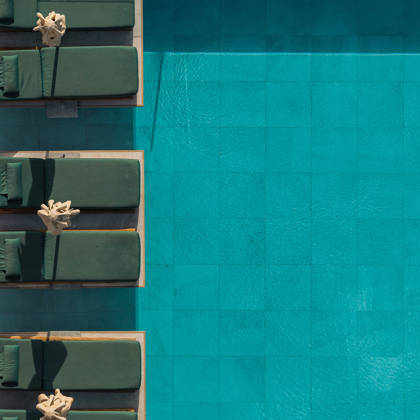 Transats verts alignés au bord de la piscine turquoise, vus d'en haut