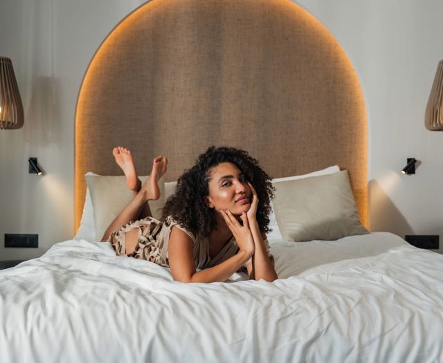 Guest relaxing on a king-size bed in a modern suite at Paralos Venus Suites in Crete.