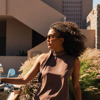 Une cliente à lunettes de soleil près d'un scooter devant l'hôtel, au soleil