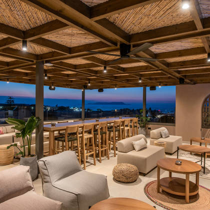 Lounge sur le toit au crépuscule avec canapés, tabourets de bar et vue sur la mer