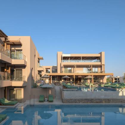 Piscine extérieure bordée de transats et parasols, encadrée par les bâtiments et les suites de l'hôtel