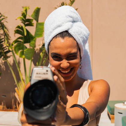 Une cliente souriante, serviette sur les cheveux, tient un appareil photo au bord de la piscine