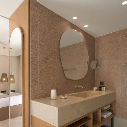 Salle de bain de Suite Junior avec vasque en pierre, miroir éclairé et grand miroir près du lit