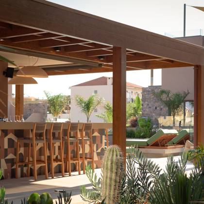 Bar au comptoir carrelé sous une pergola en bois, entouré de cactus et de transats