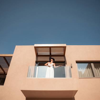 Femme en robe blanche sur le balcon ombragé d'une suite, sous un ciel bleu et dégagé