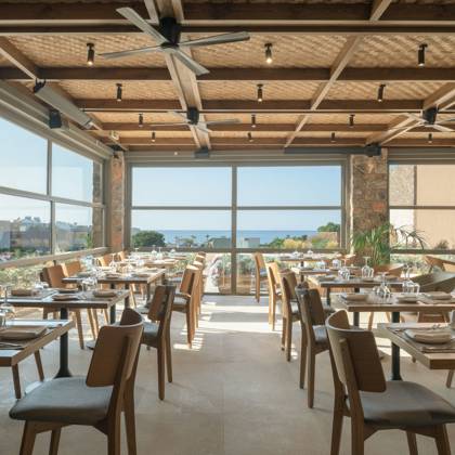Salle de restaurant avec plafond en bois, piliers en pierre et grandes baies sur la mer