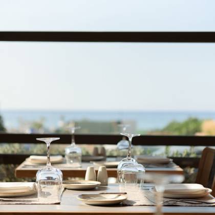 Table dressée avec verres et assiettes devant une grande baie vitrée face à la mer
