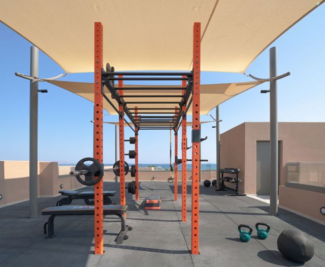 Dach-Gym mit Rack, Bank, Kettlebells und Gewichten unter Sonnensegeln am Meer