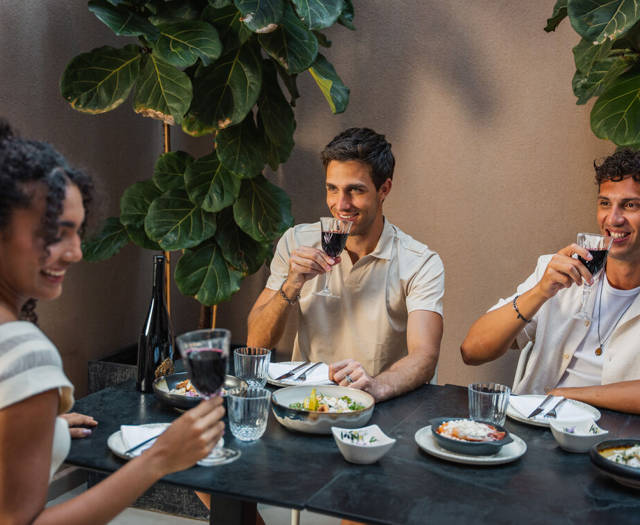 Guests enjoying red wine and à la carte dishes at a table among green plants