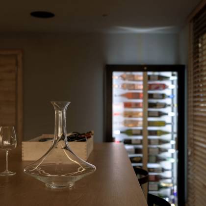 Carafe et verres à vin sur un comptoir en bois devant une cave vitrée éclairée