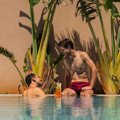 Deux clients discutent autour d'un cocktail au bord de la piscine, entourés de plantes