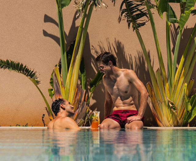 Zwei Gäste unterhalten sich bei einem Cocktail am Poolrand zwischen grünen Pflanzen