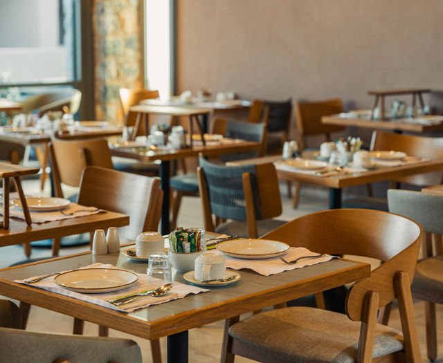 Für das Frühstück gedeckte Holztische im hellen Hauptrestaurant