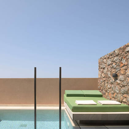 Lit de repos avec serviettes près de la piscine privée d'une Suite Junior, contre un mur en pierre