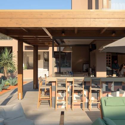 Comptoir de bar et tabourets hauts sous une pergola en bois, près des lits de repos