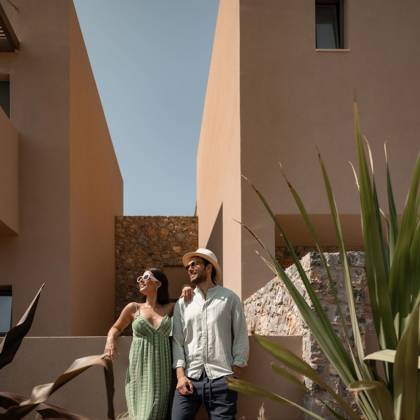 Couple souriant marchant entre les bâtiments de l'hôtel sur une allée de jardin ensoleillée