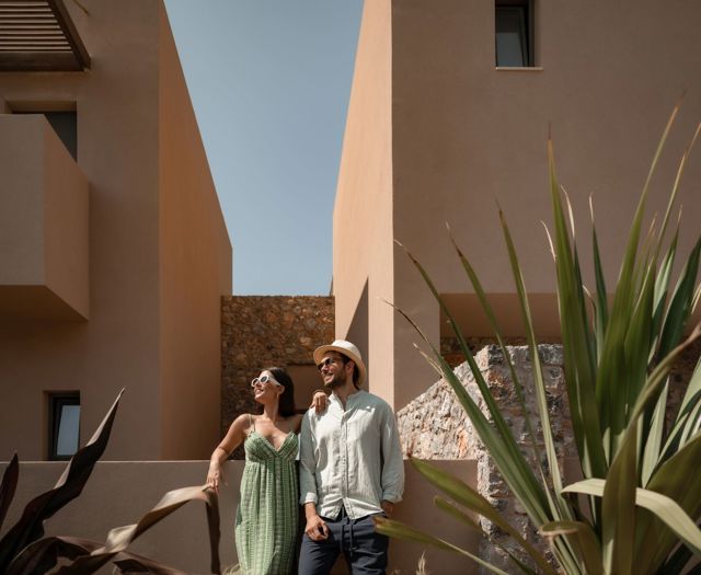 Couple souriant marchant entre les bâtiments de l'hôtel sur une allée de jardin ensoleillée