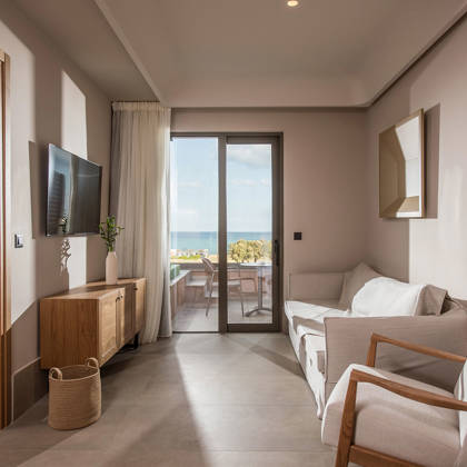 Salon de la suite avec canapé, fauteuil et télévision, ouvrant sur la terrasse avec vue mer