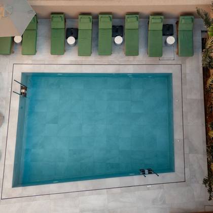 Vue aérienne d'une piscine rectangulaire bordée de transats verts et de palmiers