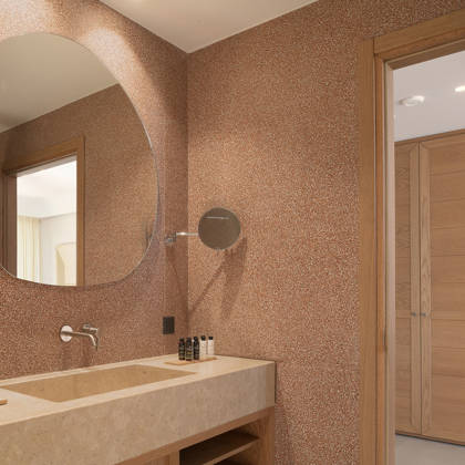 Salle de bain de la suite avec vasque en pierre, miroir rond et porte en bois vers la chambre
