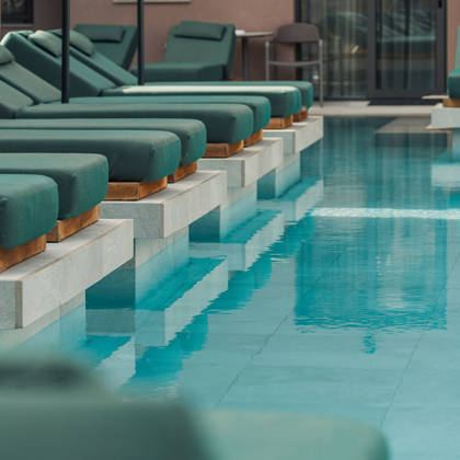 Transats verts se reflétant dans l'eau turquoise et calme de la piscine principale