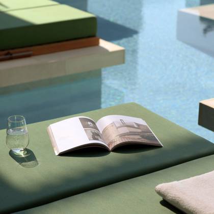Magazine ouvert, verre d'eau et serviette sur un lit de repos au bord de la piscine Swim Up