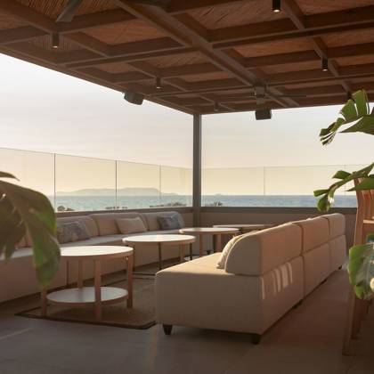 Coin lounge avec tables rondes et plantes vertes, ouvert sur la mer et les collines