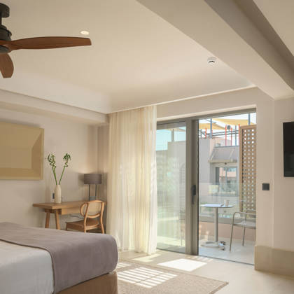 Suite Junior avec bureau en bois, télévision et ventilateur, ouvrant sur un balcon avec table