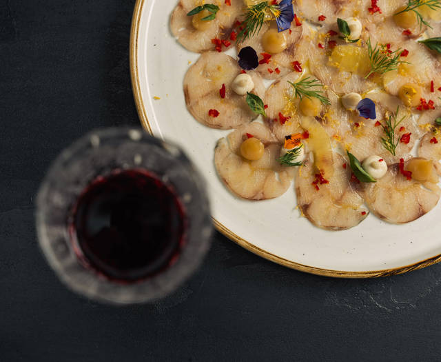 Fish carpaccio with fresh herbs and edible flowers next to a glass of red wine