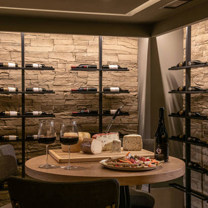 Cave à vin avec bouteilles sur murs en pierre et table dressée de fromages et vin rouge
