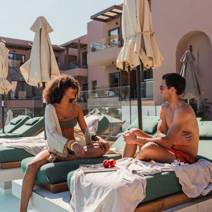 Deux clients discutent sur un lit de repos au bord de la piscine, cocktails et parasols autour d'eux