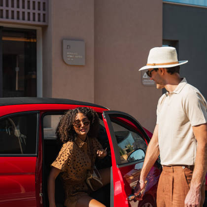 Deux clients avec une voiture de location rouge devant l'entrée de l'hôtel par une journée ensoleillée