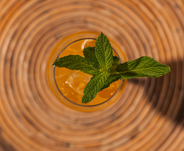 Orange cocktail topped with fresh mint, seen from above on a woven table