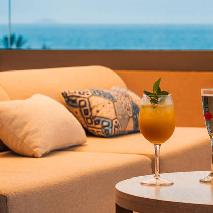 Deux cocktails sur une table basse près d'un canapé, la mer ouverte en arrière-plan