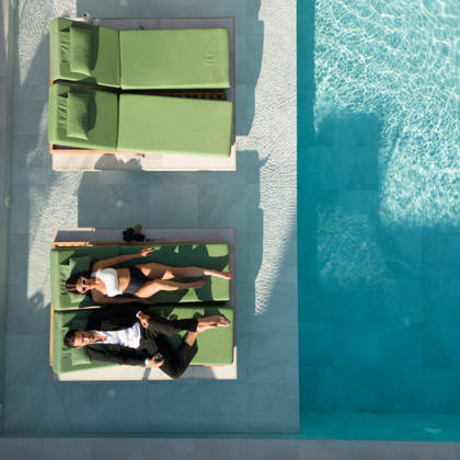 Vue aérienne de deux clients sur des transats verts au bord de la piscine turquoise