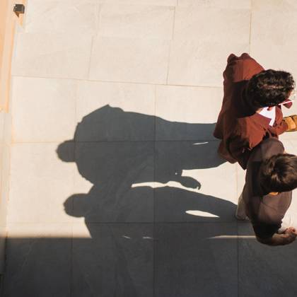 Two guests walking across a sunlit terrace at Paralos Venus Suites, casting long afternoon shadows.