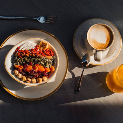 Bol de yaourt aux graines et fruits secs, accompagné d'un café et d'un jus d'orange