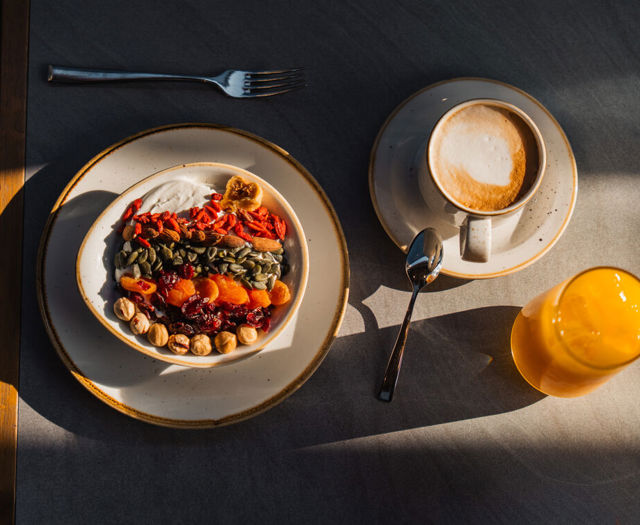 Yoghurt bowl with seeds and dried fruit next to a coffee and fresh orange juice